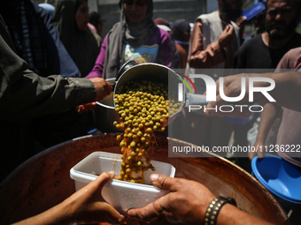 Displaced Palestinians are receiving food portions from a large pot at a public kitchen in Deir el-Balah in the central Gaza Strip on May 13...