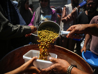 Displaced Palestinians are receiving food portions from a large pot at a public kitchen in Deir el-Balah in the central Gaza Strip on May 13...