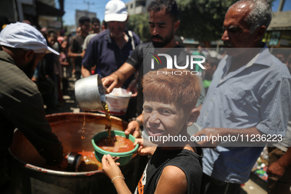 Displaced Palestinians are receiving food portions from a large pot at a public kitchen in Deir el-Balah in the central Gaza Strip on May 13...