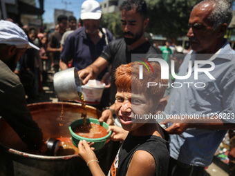 Displaced Palestinians are receiving food portions from a large pot at a public kitchen in Deir el-Balah in the central Gaza Strip on May 13...