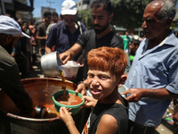 Displaced Palestinians are receiving food portions from a large pot at a public kitchen in Deir el-Balah in the central Gaza Strip on May 13...