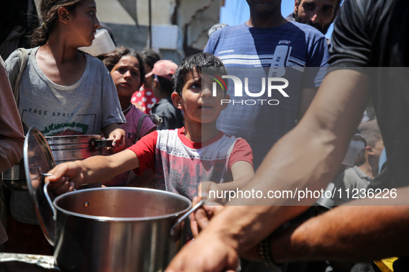 Displaced Palestinians are receiving food portions from a large pot at a public kitchen in Deir el-Balah in the central Gaza Strip on May 13...