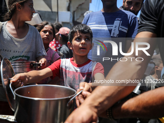 Displaced Palestinians are receiving food portions from a large pot at a public kitchen in Deir el-Balah in the central Gaza Strip on May 13...