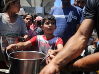 Displaced Palestinians are receiving food portions from a large pot at a public kitchen in Deir el-Balah in the central Gaza Strip on May 13...