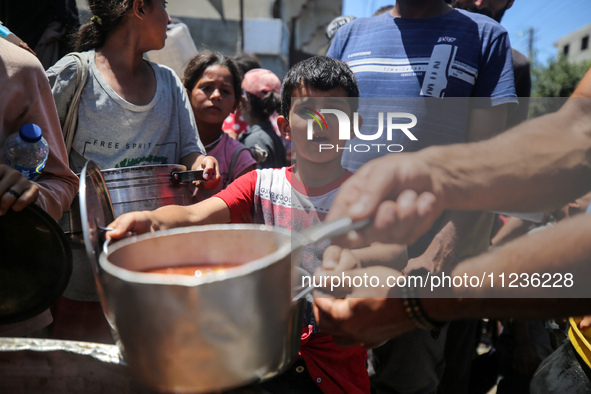 Displaced Palestinians are receiving food portions from a large pot at a public kitchen in Deir el-Balah in the central Gaza Strip on May 13...