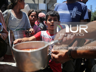 Displaced Palestinians are receiving food portions from a large pot at a public kitchen in Deir el-Balah in the central Gaza Strip on May 13...