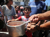 Displaced Palestinians are receiving food portions from a large pot at a public kitchen in Deir el-Balah in the central Gaza Strip on May 13...