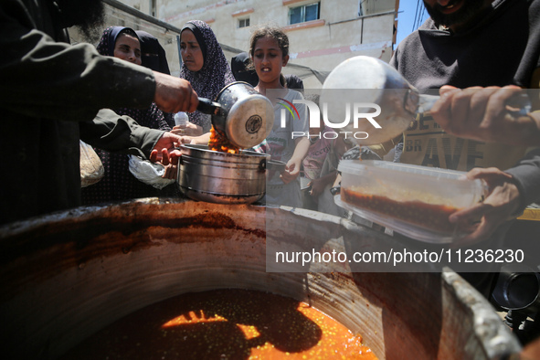 Displaced Palestinians are receiving food portions from a large pot at a public kitchen in Deir el-Balah in the central Gaza Strip on May 13...