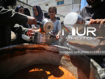 Displaced Palestinians are receiving food portions from a large pot at a public kitchen in Deir el-Balah in the central Gaza Strip on May 13...