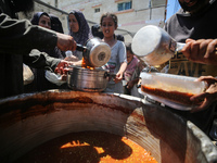 Displaced Palestinians are receiving food portions from a large pot at a public kitchen in Deir el-Balah in the central Gaza Strip on May 13...