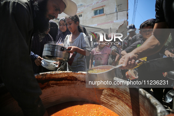 Displaced Palestinians are receiving food portions from a large pot at a public kitchen in Deir el-Balah in the central Gaza Strip on May 13...