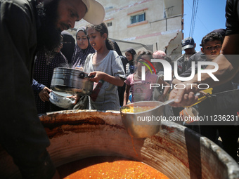 Displaced Palestinians are receiving food portions from a large pot at a public kitchen in Deir el-Balah in the central Gaza Strip on May 13...