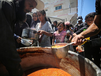 Displaced Palestinians are receiving food portions from a large pot at a public kitchen in Deir el-Balah in the central Gaza Strip on May 13...