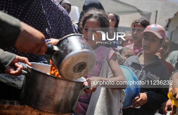 Displaced Palestinians are receiving food portions from a large pot at a public kitchen in Deir el-Balah in the central Gaza Strip on May 13...