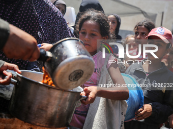 Displaced Palestinians are receiving food portions from a large pot at a public kitchen in Deir el-Balah in the central Gaza Strip on May 13...