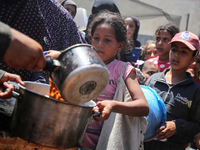 Displaced Palestinians are receiving food portions from a large pot at a public kitchen in Deir el-Balah in the central Gaza Strip on May 13...