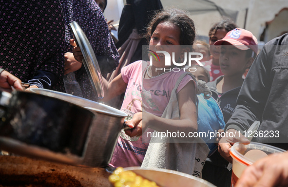 Displaced Palestinians are receiving food portions from a large pot at a public kitchen in Deir el-Balah in the central Gaza Strip on May 13...