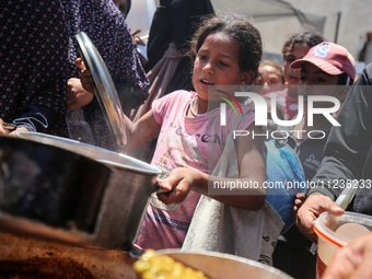 Displaced Palestinians are receiving food portions from a large pot at a public kitchen in Deir el-Balah in the central Gaza Strip on May 13...