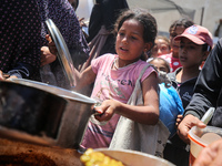 Displaced Palestinians are receiving food portions from a large pot at a public kitchen in Deir el-Balah in the central Gaza Strip on May 13...