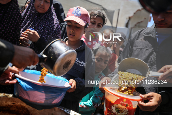 Displaced Palestinians are receiving food portions from a large pot at a public kitchen in Deir el-Balah in the central Gaza Strip on May 13...