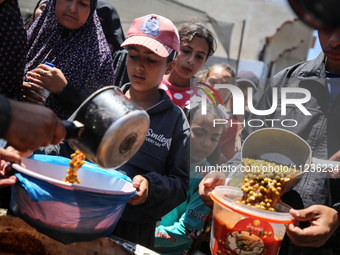 Displaced Palestinians are receiving food portions from a large pot at a public kitchen in Deir el-Balah in the central Gaza Strip on May 13...