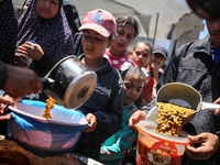 Displaced Palestinians are receiving food portions from a large pot at a public kitchen in Deir el-Balah in the central Gaza Strip on May 13...