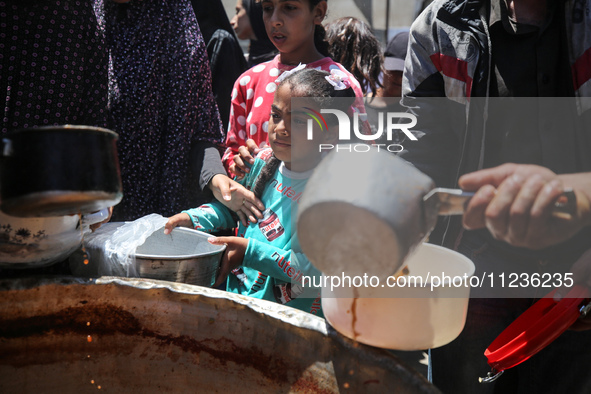 Displaced Palestinians are receiving food portions from a large pot at a public kitchen in Deir el-Balah in the central Gaza Strip on May 13...