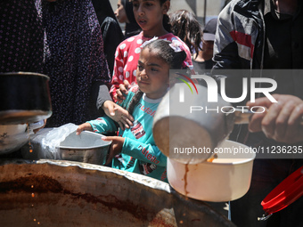 Displaced Palestinians are receiving food portions from a large pot at a public kitchen in Deir el-Balah in the central Gaza Strip on May 13...