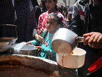 Displaced Palestinians are receiving food portions from a large pot at a public kitchen in Deir el-Balah in the central Gaza Strip on May 13...