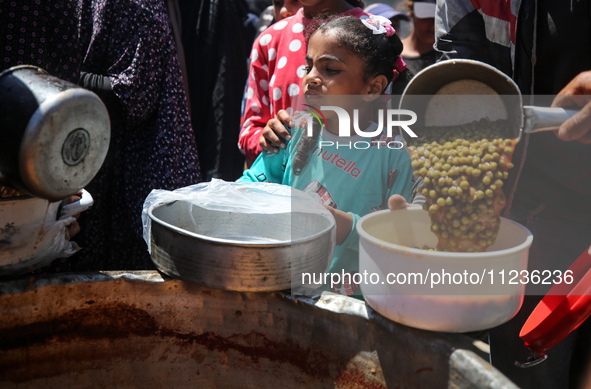 Displaced Palestinians are receiving food portions from a large pot at a public kitchen in Deir el-Balah in the central Gaza Strip on May 13...