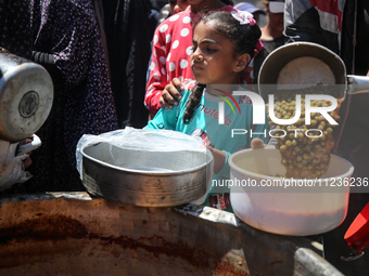 Displaced Palestinians are receiving food portions from a large pot at a public kitchen in Deir el-Balah in the central Gaza Strip on May 13...