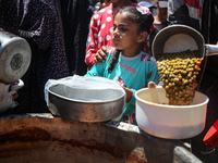 Displaced Palestinians are receiving food portions from a large pot at a public kitchen in Deir el-Balah in the central Gaza Strip on May 13...