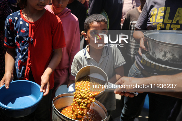 Displaced Palestinians are receiving food portions from a large pot at a public kitchen in Deir el-Balah in the central Gaza Strip on May 13...