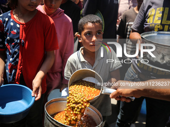 Displaced Palestinians are receiving food portions from a large pot at a public kitchen in Deir el-Balah in the central Gaza Strip on May 13...