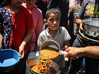 Displaced Palestinians are receiving food portions from a large pot at a public kitchen in Deir el-Balah in the central Gaza Strip on May 13...