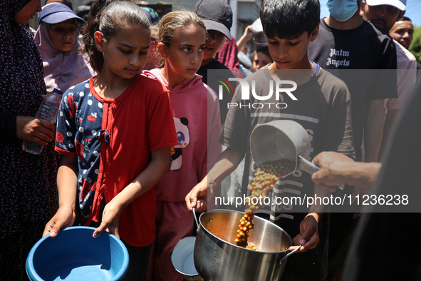 Displaced Palestinians are receiving food portions from a large pot at a public kitchen in Deir el-Balah in the central Gaza Strip on May 13...