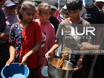 Displaced Palestinians are receiving food portions from a large pot at a public kitchen in Deir el-Balah in the central Gaza Strip on May 13...