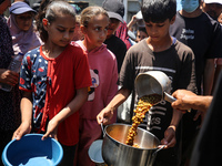 Displaced Palestinians are receiving food portions from a large pot at a public kitchen in Deir el-Balah in the central Gaza Strip on May 13...