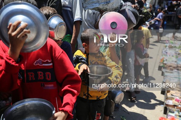 Displaced Palestinians are queuing to receive food rations from a public kitchen in Deir el-Balah in the central Gaza Strip on May 13, 2024,...