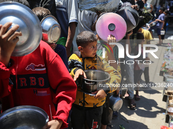 Displaced Palestinians are queuing to receive food rations from a public kitchen in Deir el-Balah in the central Gaza Strip on May 13, 2024,...