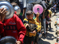 Displaced Palestinians are queuing to receive food rations from a public kitchen in Deir el-Balah in the central Gaza Strip on May 13, 2024,...