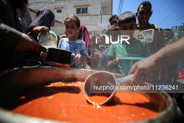 Displaced Palestinians are receiving food portions from a large pot at a public kitchen in Deir el-Balah in the central Gaza Strip on May 13...