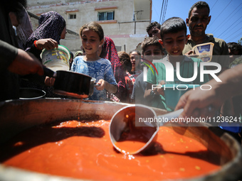 Displaced Palestinians are receiving food portions from a large pot at a public kitchen in Deir el-Balah in the central Gaza Strip on May 13...