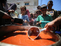 Displaced Palestinians are receiving food portions from a large pot at a public kitchen in Deir el-Balah in the central Gaza Strip on May 13...