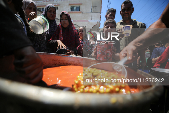 Displaced Palestinians are receiving food portions from a large pot at a public kitchen in Deir el-Balah in the central Gaza Strip on May 13...