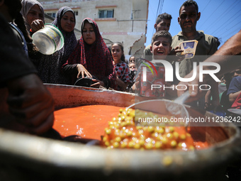 Displaced Palestinians are receiving food portions from a large pot at a public kitchen in Deir el-Balah in the central Gaza Strip on May 13...