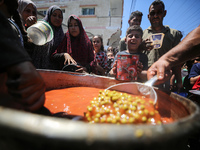 Displaced Palestinians are receiving food portions from a large pot at a public kitchen in Deir el-Balah in the central Gaza Strip on May 13...