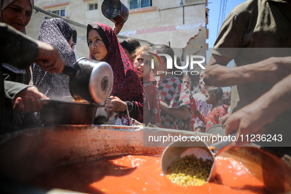 Displaced Palestinians are receiving food portions from a large pot at a public kitchen in Deir el-Balah in the central Gaza Strip on May 13...