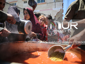 Displaced Palestinians are receiving food portions from a large pot at a public kitchen in Deir el-Balah in the central Gaza Strip on May 13...