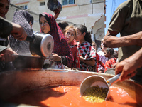 Displaced Palestinians are receiving food portions from a large pot at a public kitchen in Deir el-Balah in the central Gaza Strip on May 13...